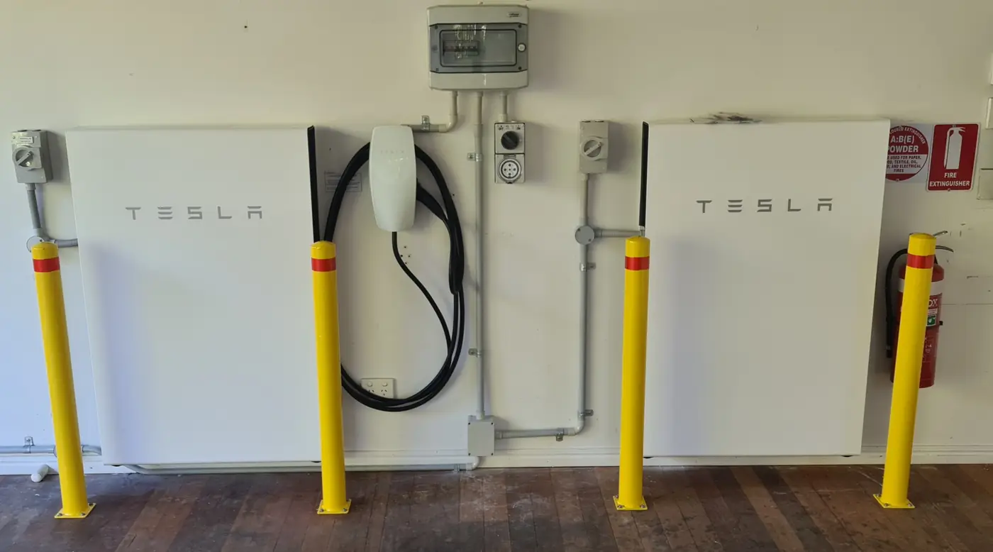 A Tesla wall connector charging cable between two wall-mounted batteries